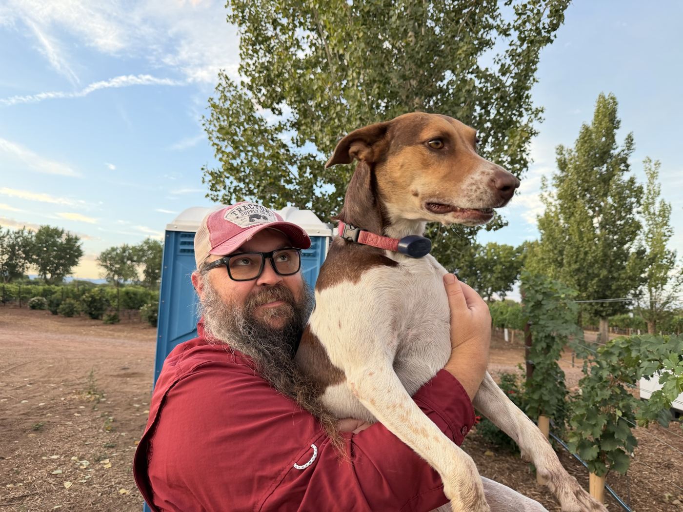 A man in a red shirt holding a happy hound dog
